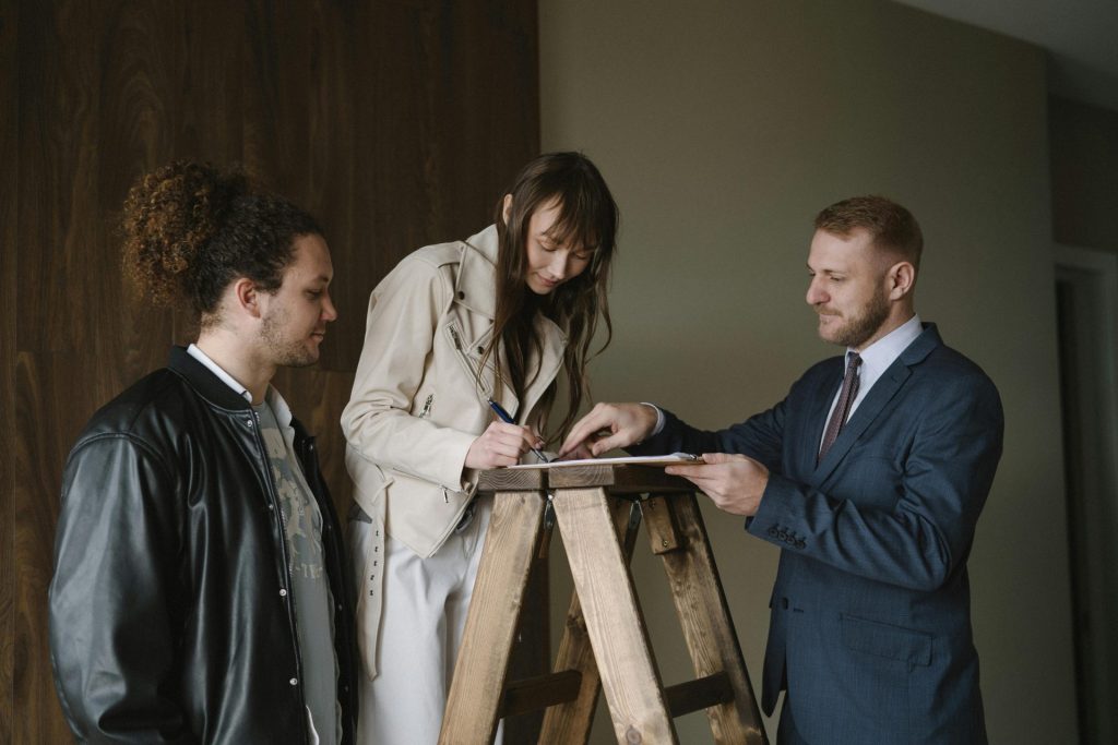 Three individuals signing a contract on a ladder inside a new house, symbolizing a real estate deal.